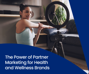 A health and wellness influencer in athletic wear stretches on a mat while looking into her phone, which is set up in a ring light.